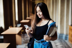 Estudante em uma biblioteca, interagindo com um smartphone enquanto segura livros, simbolizando a união da educação tradicional e a inovação digital através da identificação online.
