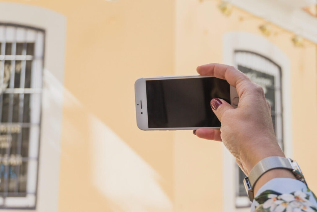 Uma mão segurando um smartphone com a tela voltada para uma fachada de edifício, destacando ‘O Papel dos Aplicativos de Vistoria’ na avaliação e documentação de propriedades através de dispositivos móveis.