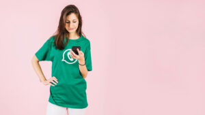 A imagem mostra uma pessoa de pé contra um fundo rosa, vestindo uma camiseta verde com um símbolo de ícone de chat branco, segurando um smartphone. Isso sugere o tema “Dicas de Mensagens para Atendimento”.