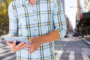 A imagem mostra uma pessoa usando um tablet em uma rua da cidade, simbolizando a mobilidade e conveniência dos aplicativos de vistoria em ambientes urbanos. A pessoa está vestida com uma camisa xadrez, o que pode indicar um ambiente de trabalho informal ou uma inspeção casual. Mostrando assim o Papel dos Aplicativos de Vistoria.