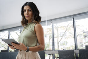 Mulher corretora usando tablet em ambiente corporativo, representando liderança feminina no mercado imobiliário.