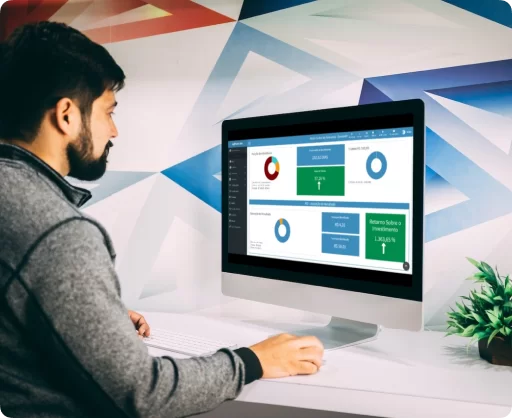Imagem de um profissional utilizando o sistema agPhoto em um computador de mesa moderno. Ele está visualizando uma interface de usuário com dashboard de métricas, que inclui gráficos de pizza e barras com informações sobre vendas, interação com clientes e retorno sobre investimento. O ambiente de trabalho sugere foco e produtividade, com um design de escritório contemporâneo e um toque de decoração verde com uma pequena planta ao lado do monitor. Este cenário destaca as funcionalidades do agPhoto como uma ferramenta abrangente para a gestão de empresas de formaturas e eventos, e a dedicação da empresa ao suporte e capacitação dos usuários do sistema.