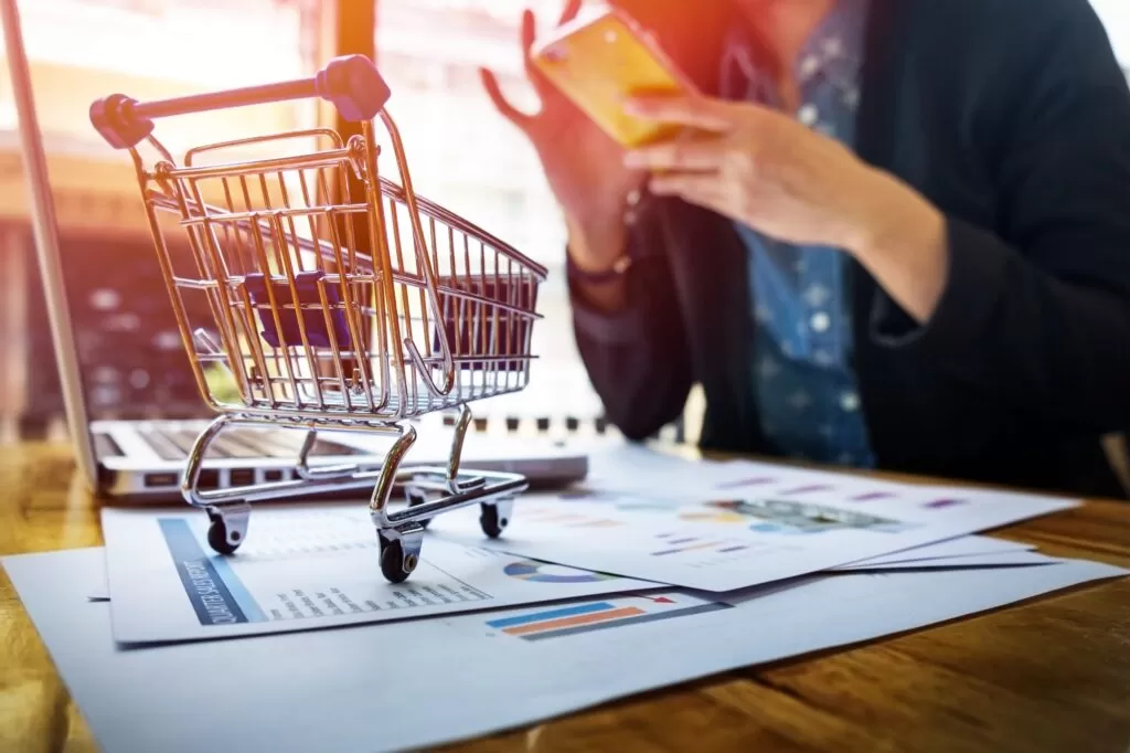 Lições das grandes marcas do varejo de moda brasileiro — carrinho de compras em miniatura sobre documentos financeiros, representando estratégias do setor varejista e inovação na gestão comercial.