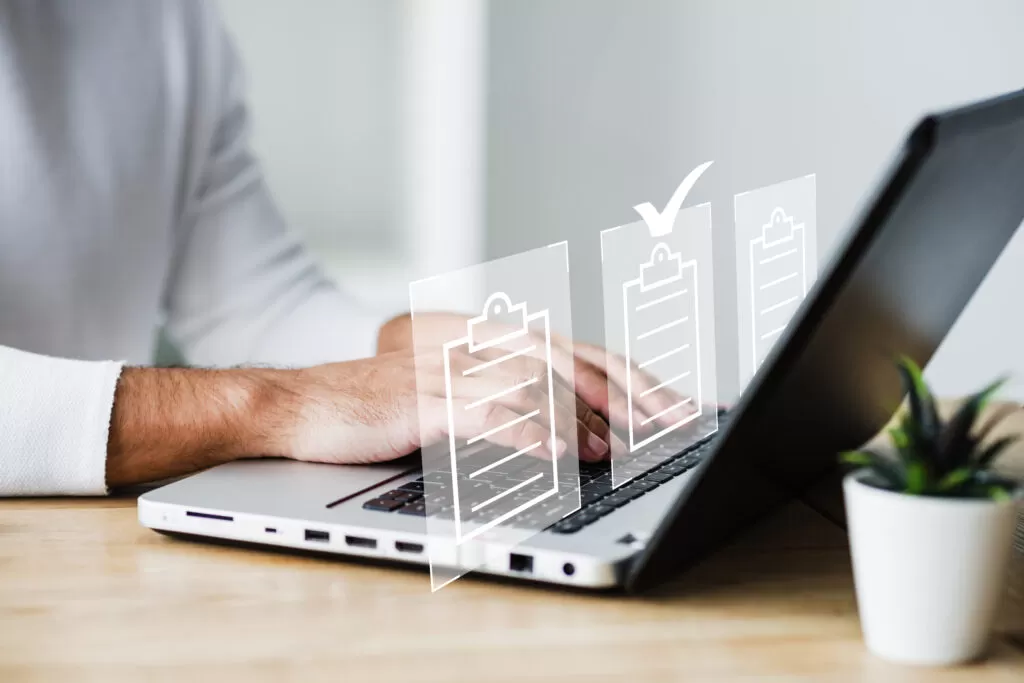 Pessoa digitando em um laptop com ícones digitais de checklist ao lado, representando a importância da atualização de dados para otimizar a gestão empresarial.