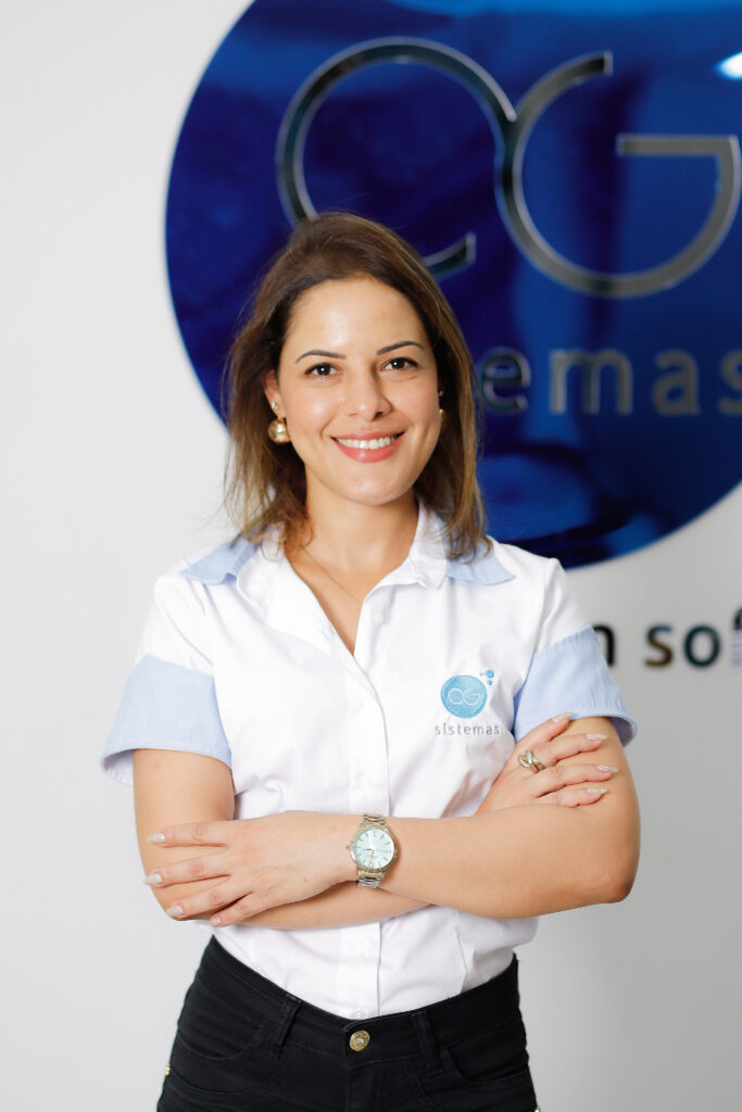 Mayara Barbosa, sorrindo e de braços cruzados, representa o comprometimento da equipe da AG Sistemas como Coordenadora de RH, refletindo a cultura acolhedora e o ambiente profissional da empresa baseada em Tupã.