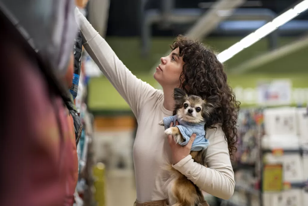 Cliente escolhendo produtos no pet shop enquanto segura seu cachorro, demonstrando como melhorar a gestão para vender mais no Pet Shop